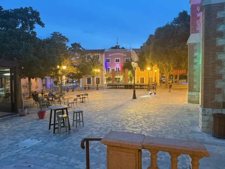 Het dorpsplein van Sainte-Marie-la-Mer bij avond, met de verlichte mairie in blauw-wit-rood en een terras op het plein